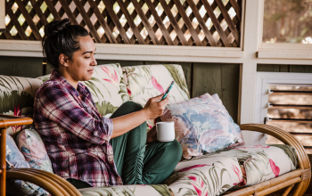 A young woman on a couch with coffee mug and mobile phone.