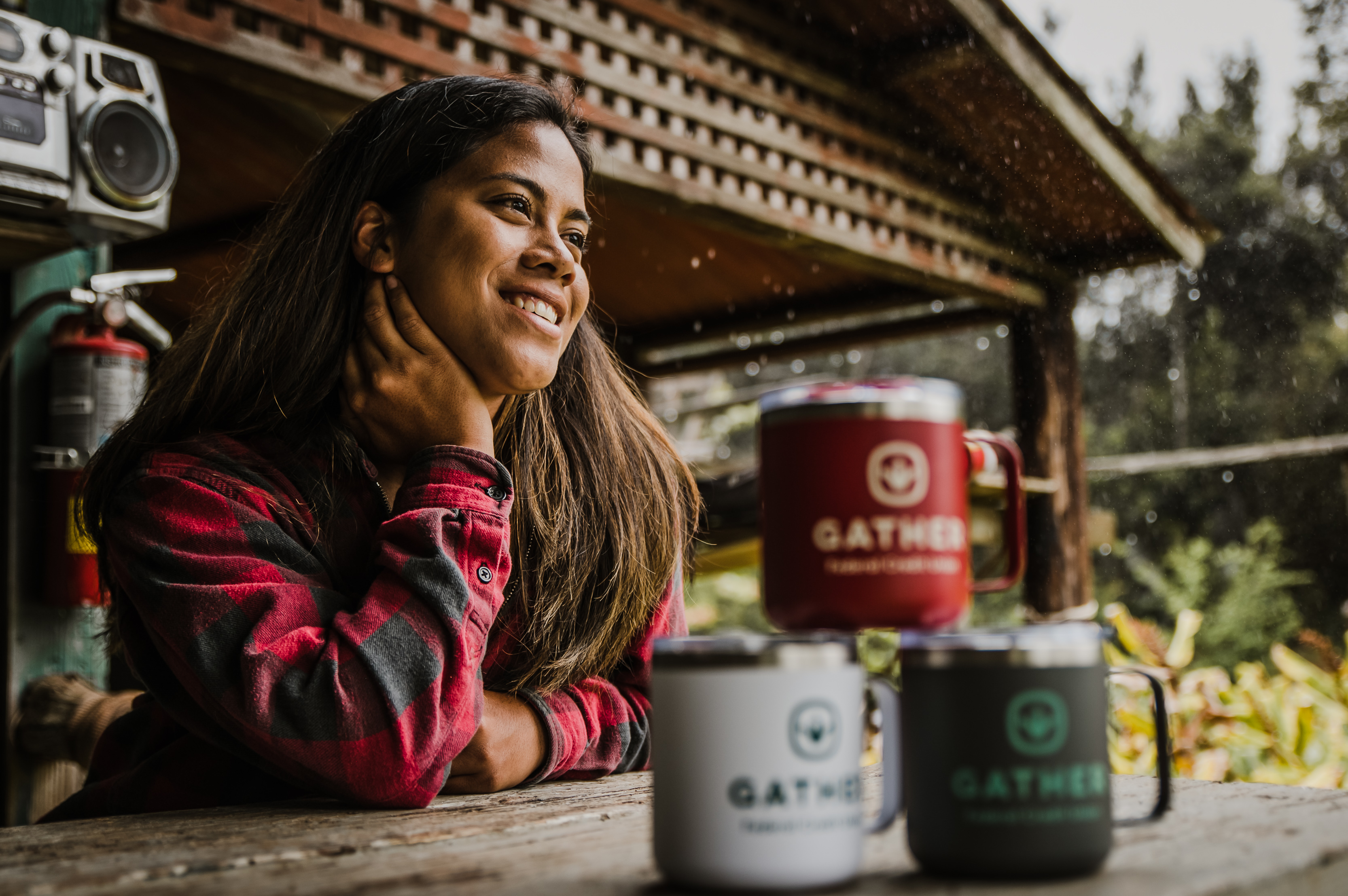 woman smiling in a red and black plaid shirt with Gather Federal Credit Union drinking mugs.