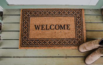 A birdseye view of a welcome mat with boots on a front porch